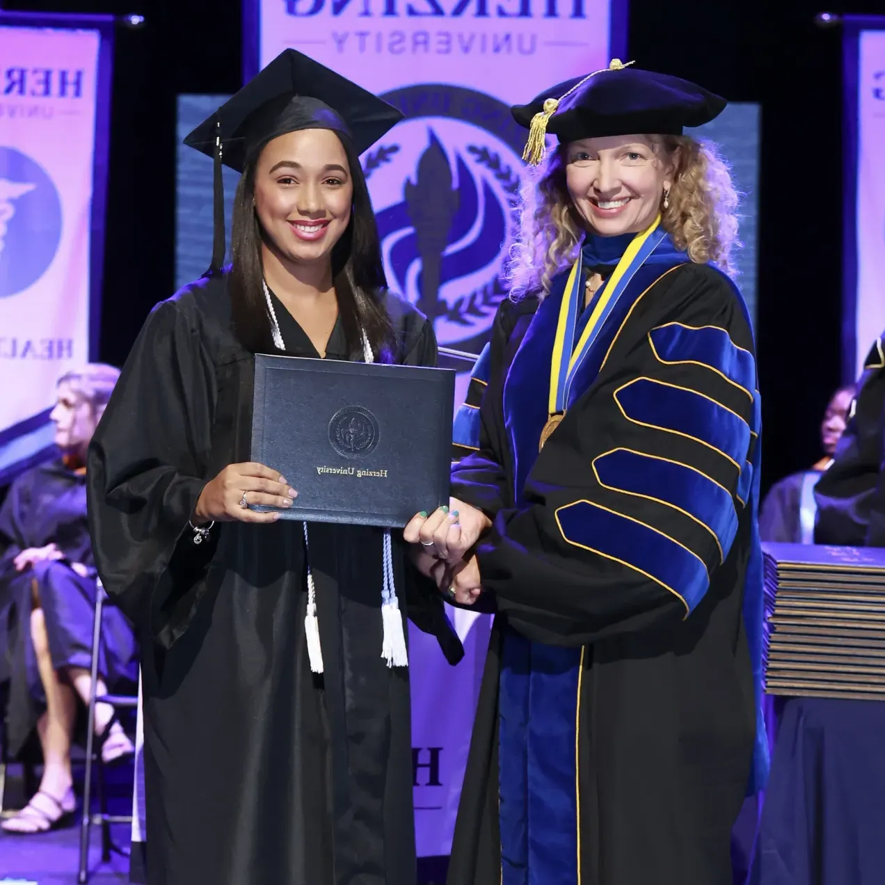 Herzing University graduate receiving their diploma on stage during a commencement ceremony.